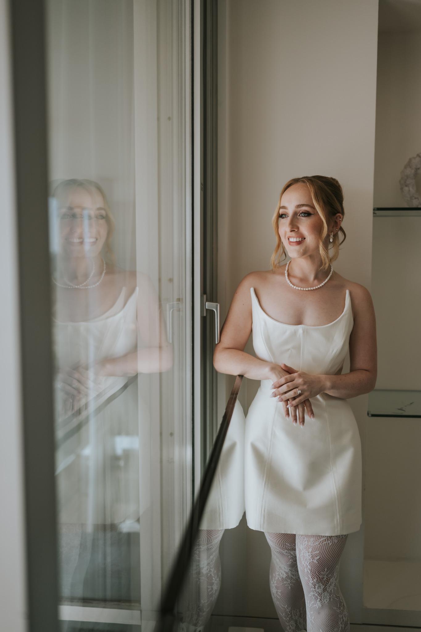 Lexi in a white bridal outfit standing by a window