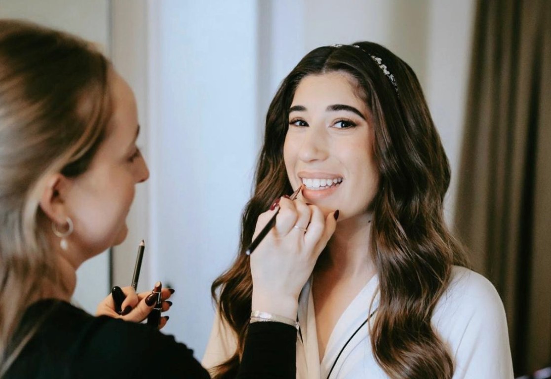 Makeup artist applying lipstick to a smiling bridal client